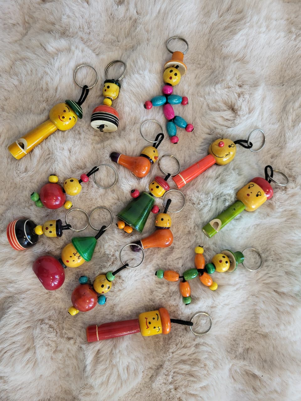 Assortment of Channapatna wooden keychain figures on white fur rug showing various designs