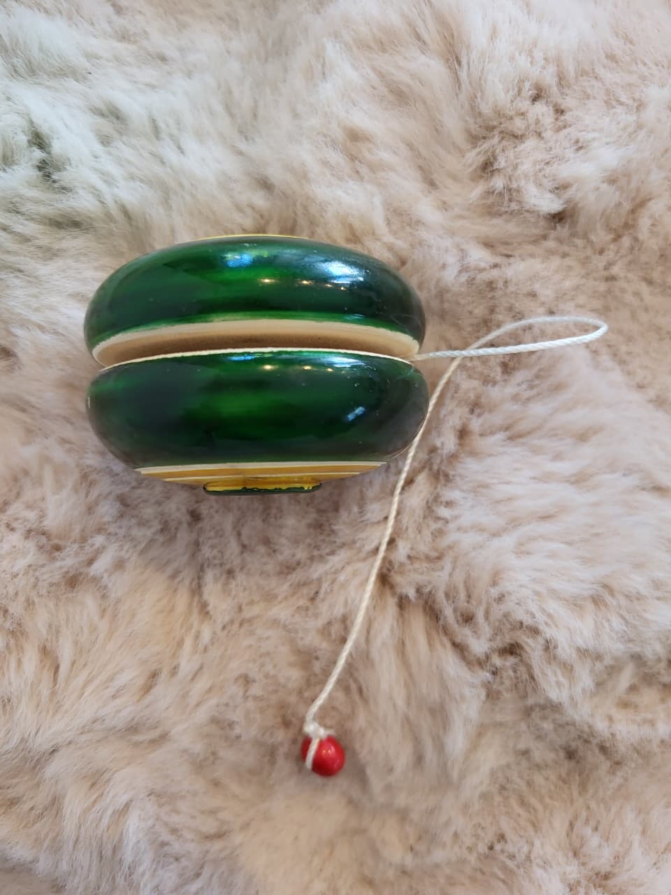Channapatna wooden yo-yo side view showing green body and yellow ring bands with red bead string