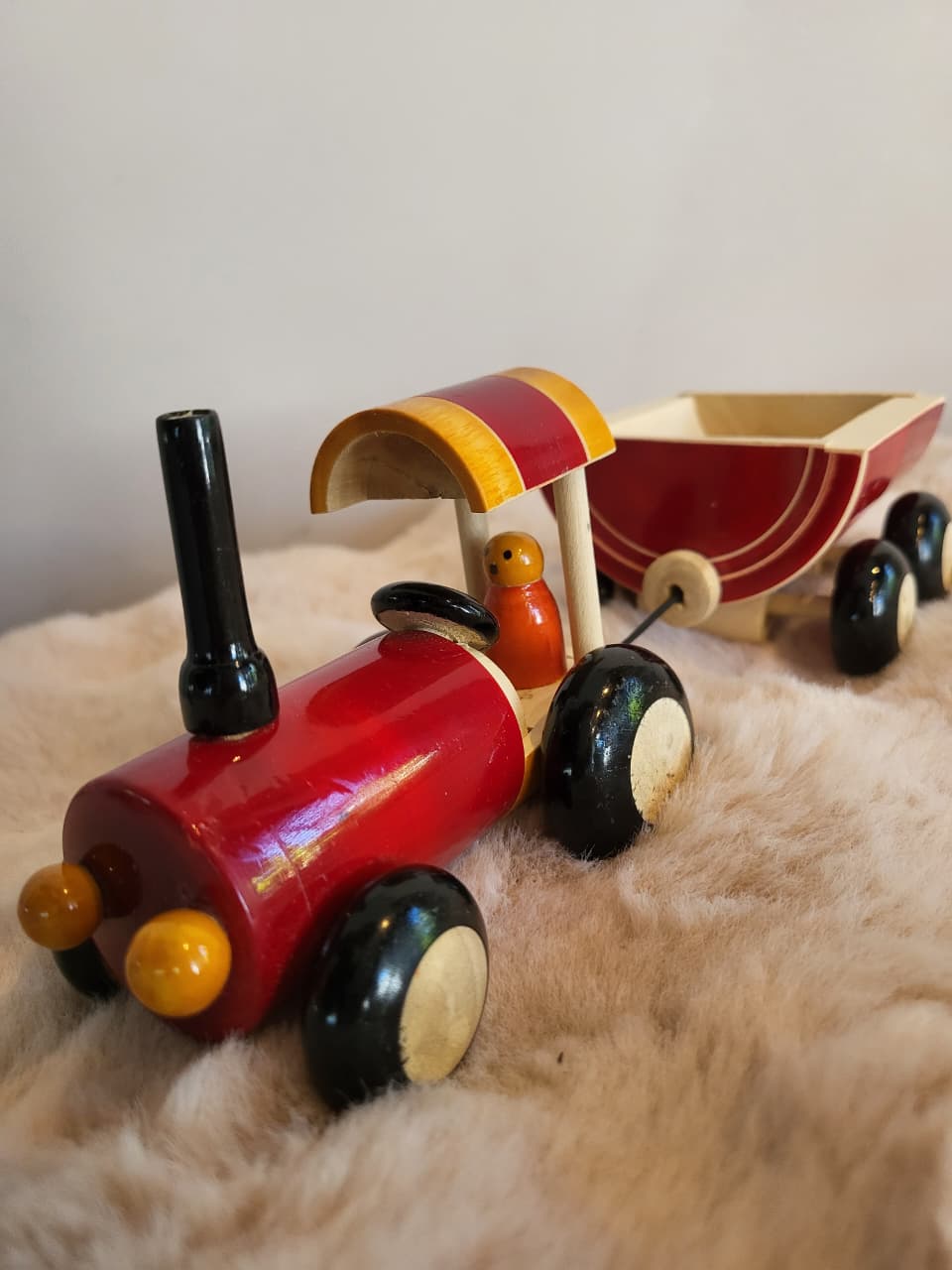 Handcrafted wooden toy tractor with red body, striped canopy and orange peg driver, with trailer