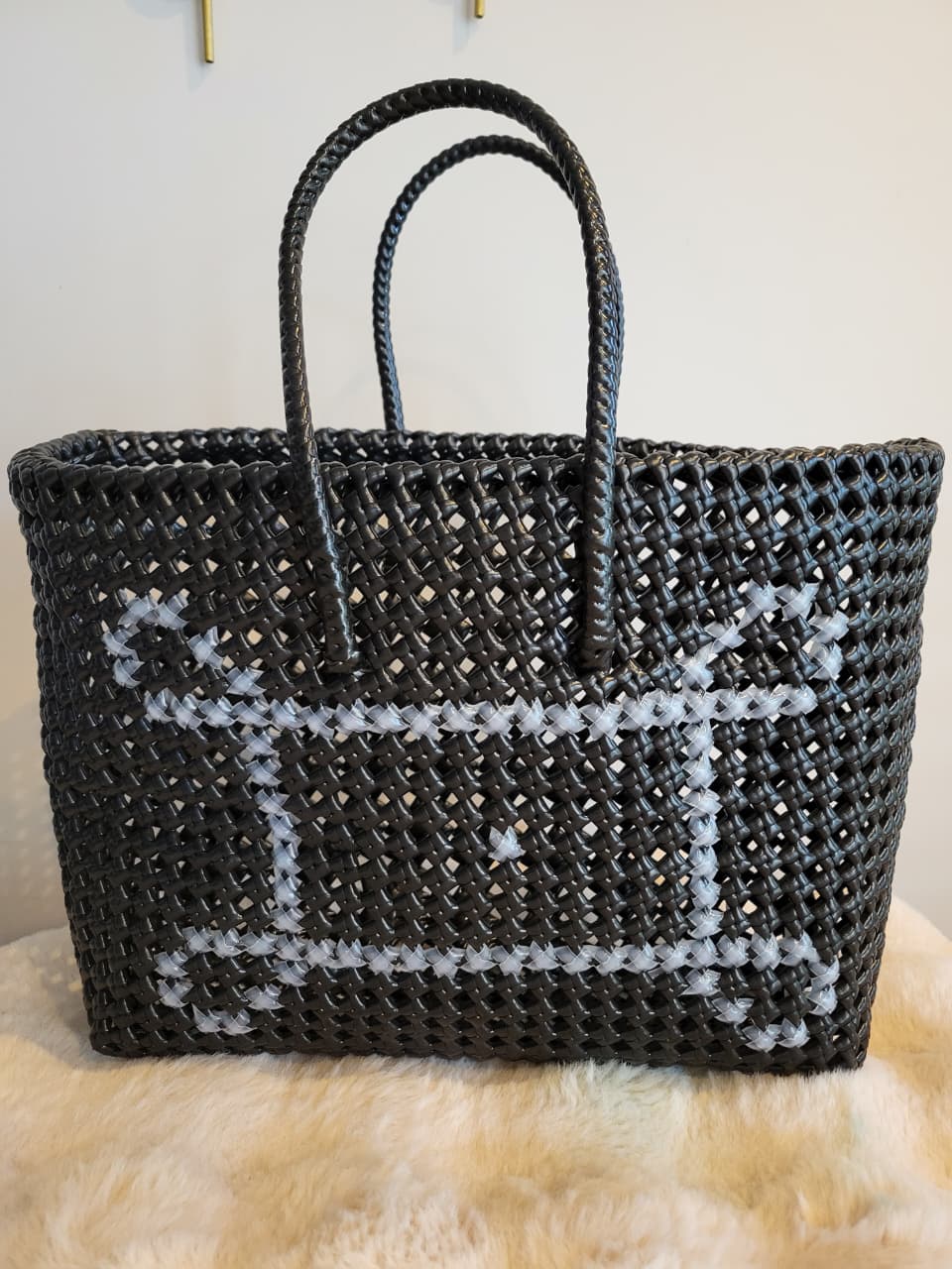 Handwoven black tote bag front view with white cross-stitch floral pattern and braided handles