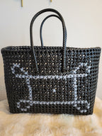 Handwoven black tote bag front view with white cross-stitch floral pattern and braided handles