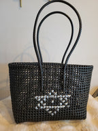 Handwoven black tote bag front view with white cross-stitch heart motif and tall braided handles