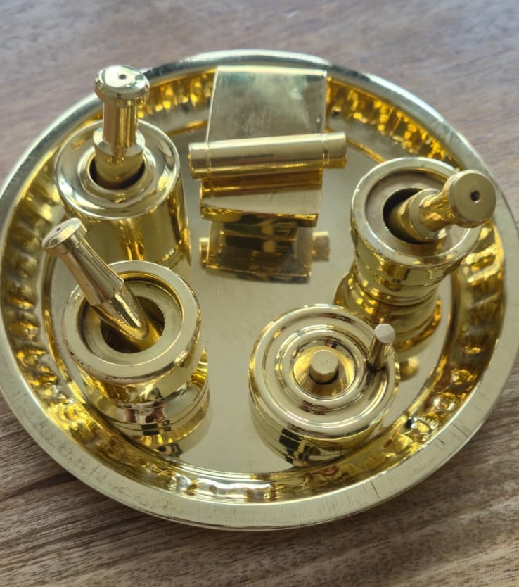Miniature brass puja thali set with glossy gold finish on wooden surface