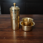 Brass filter coffee maker set with tumbler on dark wood surface