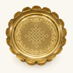 Overhead view of brass uruli with kolam engraving on ivory background