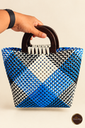 Hand-held front view of small blue-black-white diamond handbag with wooden handles