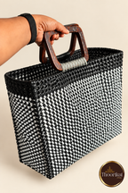 Hand-held angled view of black-white handwoven market bag with wooden handles