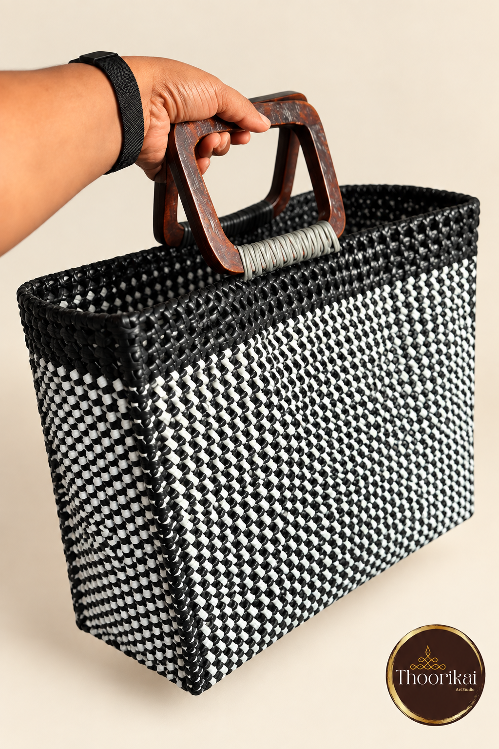 Hand-held angled view of black-white handwoven market bag with wooden handles
